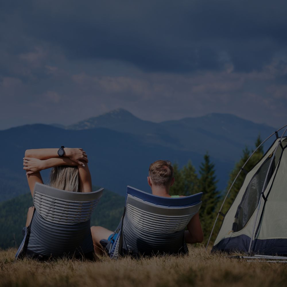 Couple sitting in camp chairs enjoying scenic mountain view beside tent